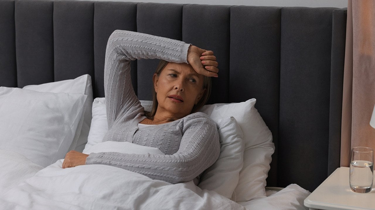 A middle-aged woman experiencing headache while sitting on bed.