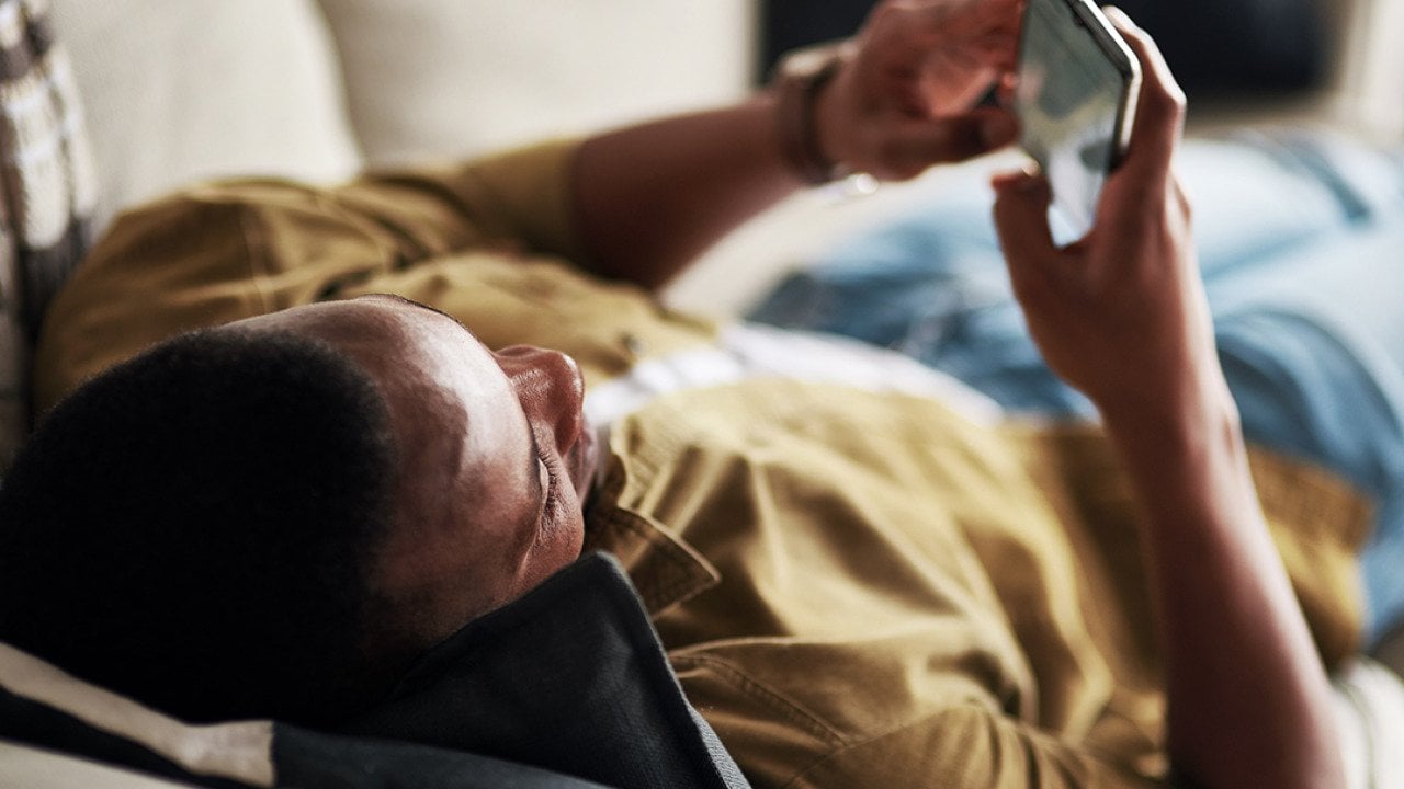 Young man relaxing on a couch at home while scrolling through social media on his phone.