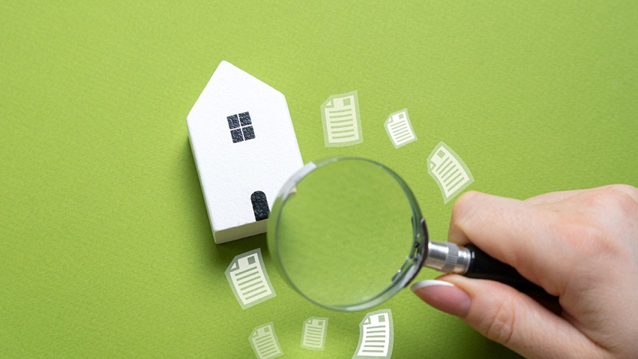A magnifying glass looking over a figure of a house on a green background.