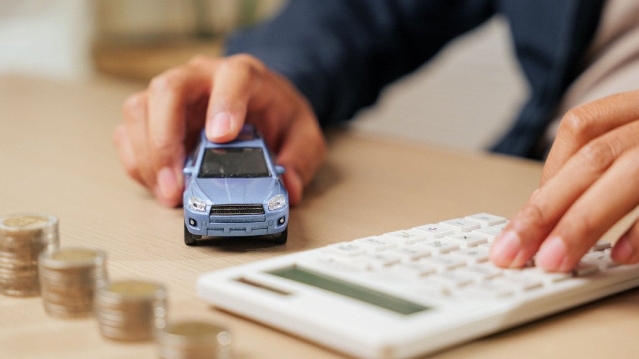 Calculator in hand as a person calculates car loan payments by a small car model and coins. 