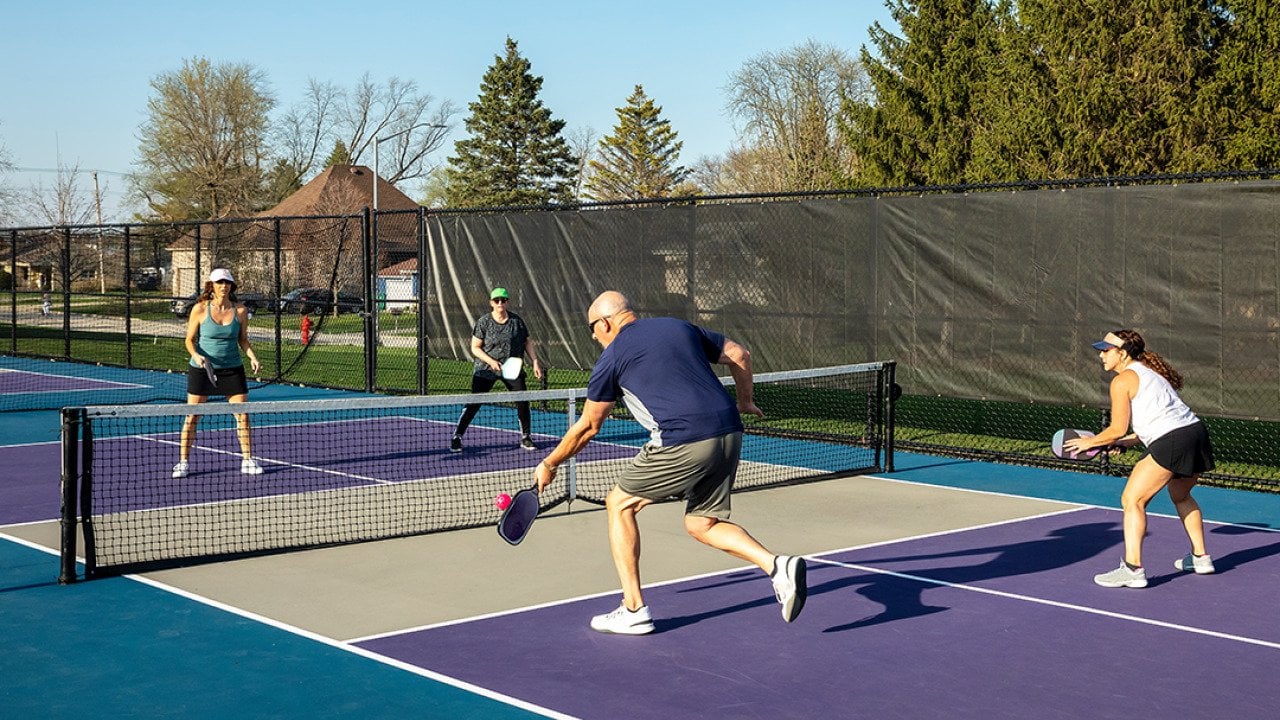 Two teams playing at a public park's pickleball court where a male player returns a volley at the net.