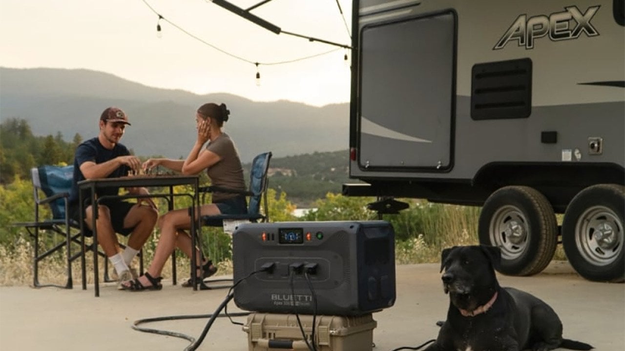 Couple at a table with a dog camping next to an RV.