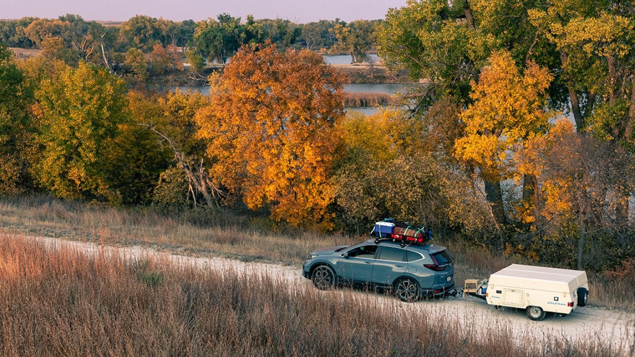 A blue 2020 Honda CR-V towing a 1990 Coleman Columbia pop-up camper on the road towards Antelope Lake in Kansas during autumn.