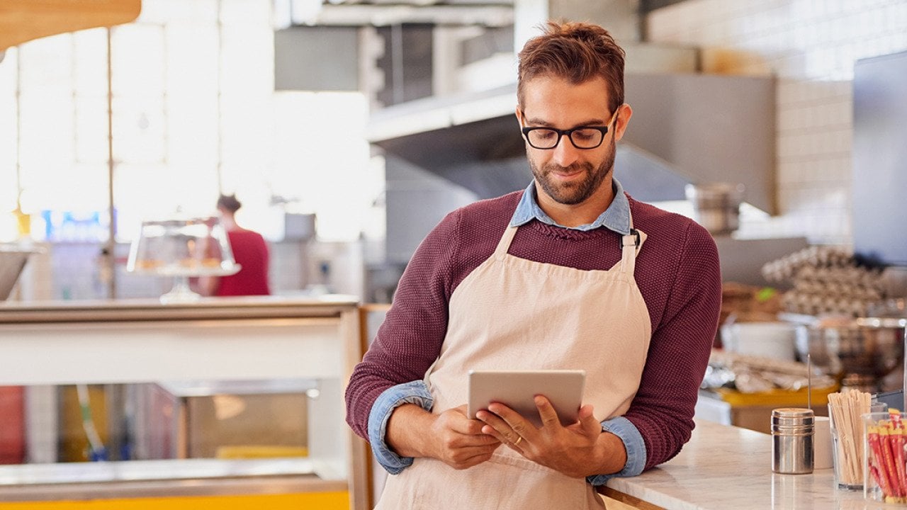 A coffee shop owner using a tablet inside the shop's kitchen.