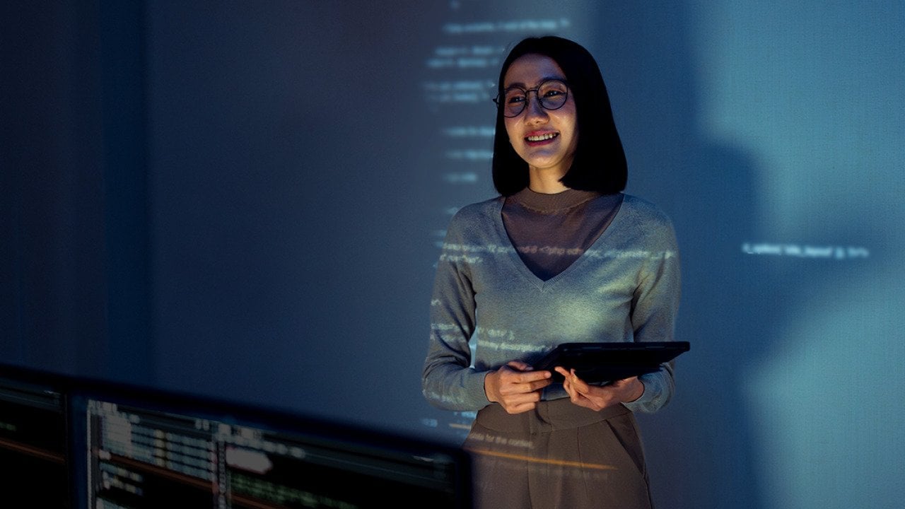 A learning & development employee standing in front of a screen where software lessons are projected.