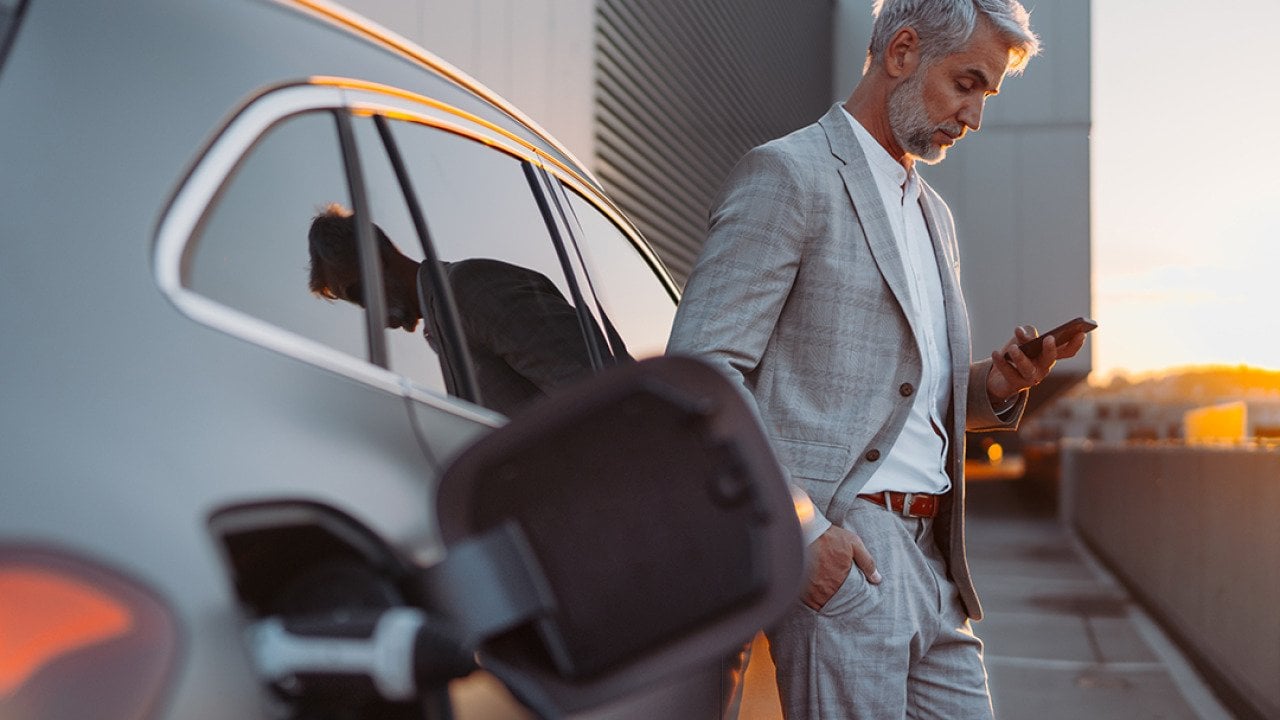 A man leaning on his electric car while using his smartphone.