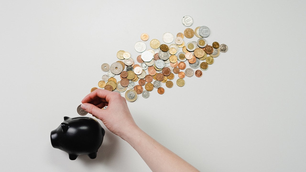 Coins being inserted into a black piggy bank.