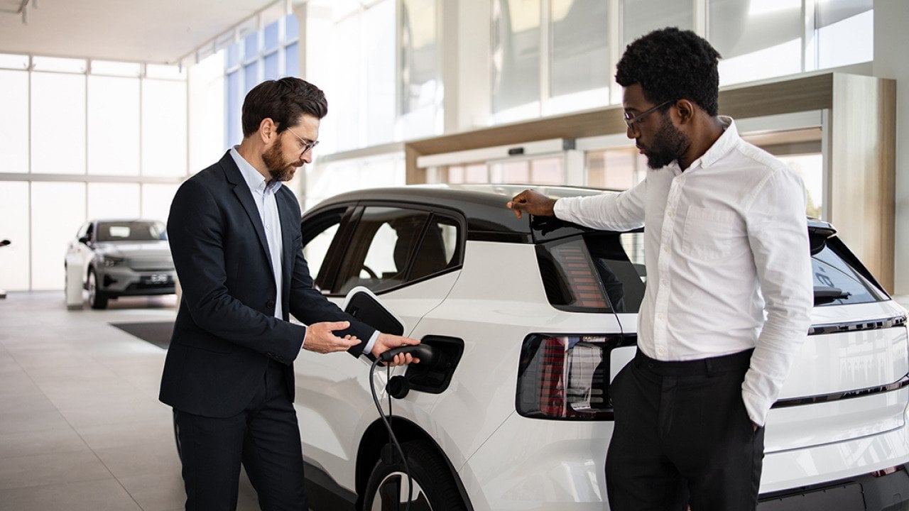 A dealer selling a white electric SUV to businessman in a car dealership.