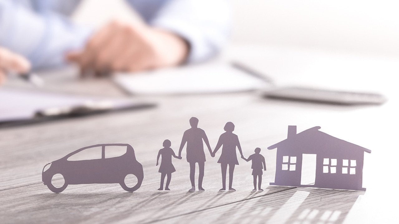 an insurance agent writing in documents with a paper figure of a family with a house and car.