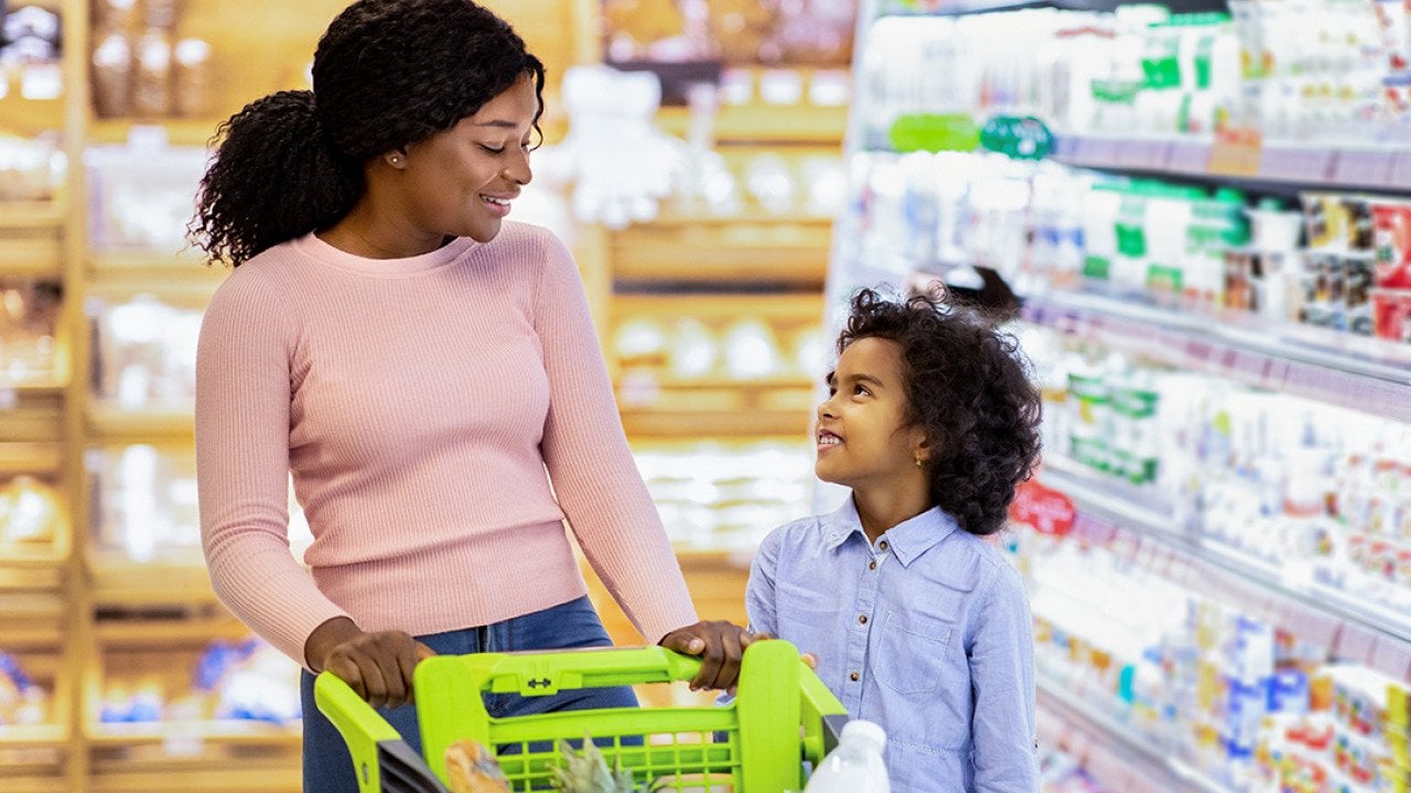 A young black mom and her daughter shopping together for groceries in a supermarket.