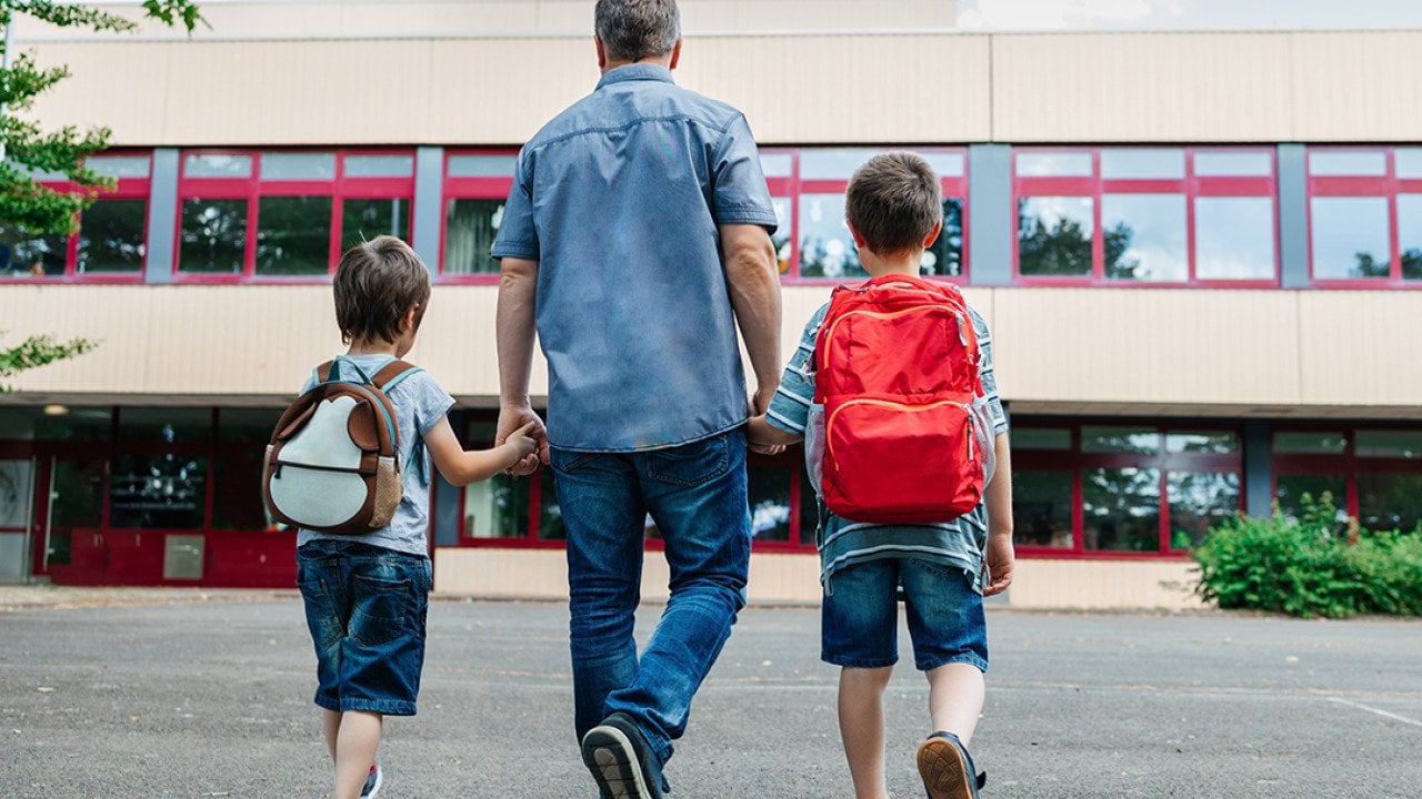A father holding his two young boys and dropping them back to school.