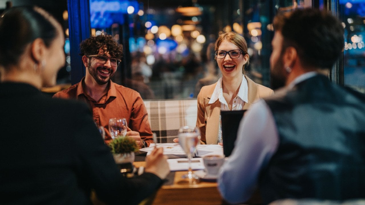 A group of business people laughing and discussing during a meeting in a modern restaurant setting. 