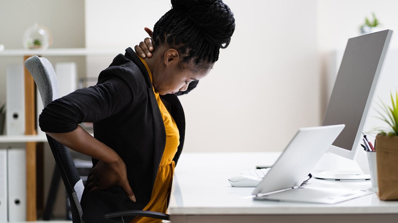A female employee sitting in her office experiencing back pains.
