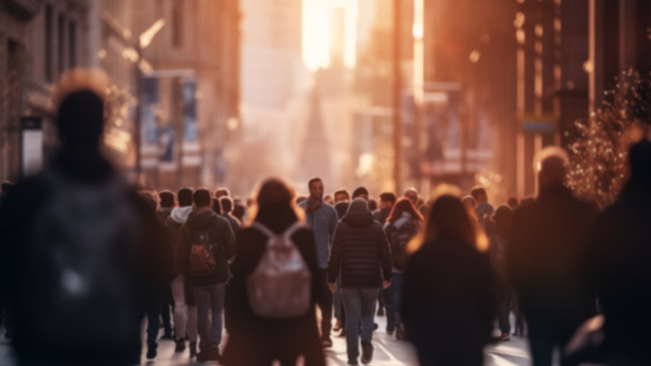 A crowd of people walking in a city street during sunset.