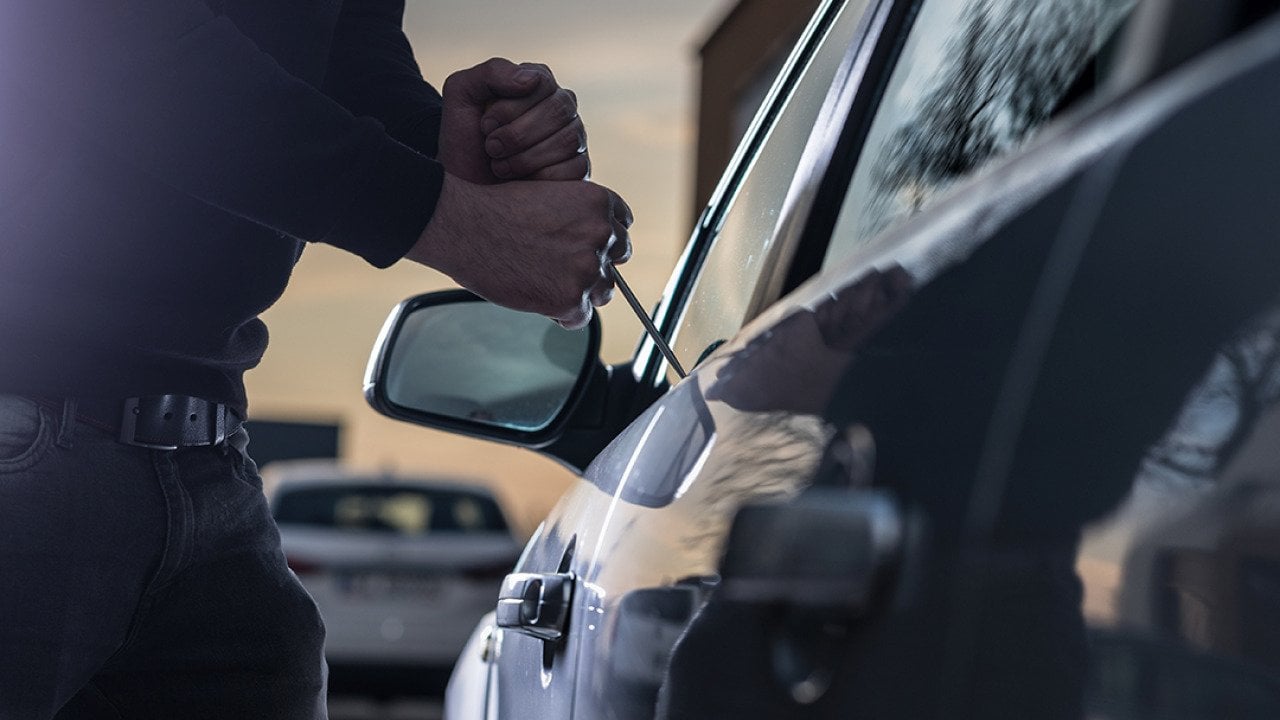 A thief trying to break into a car window with a screwdriver.