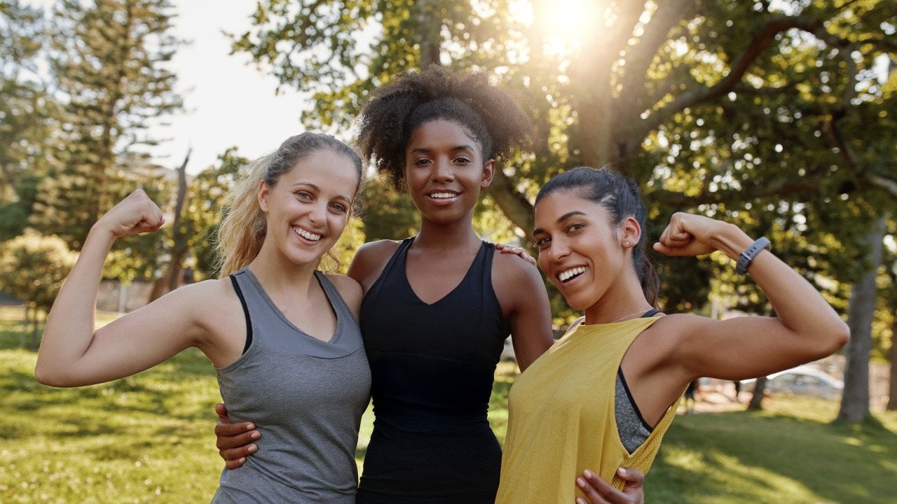 Three women flexing their muscles in a park.
