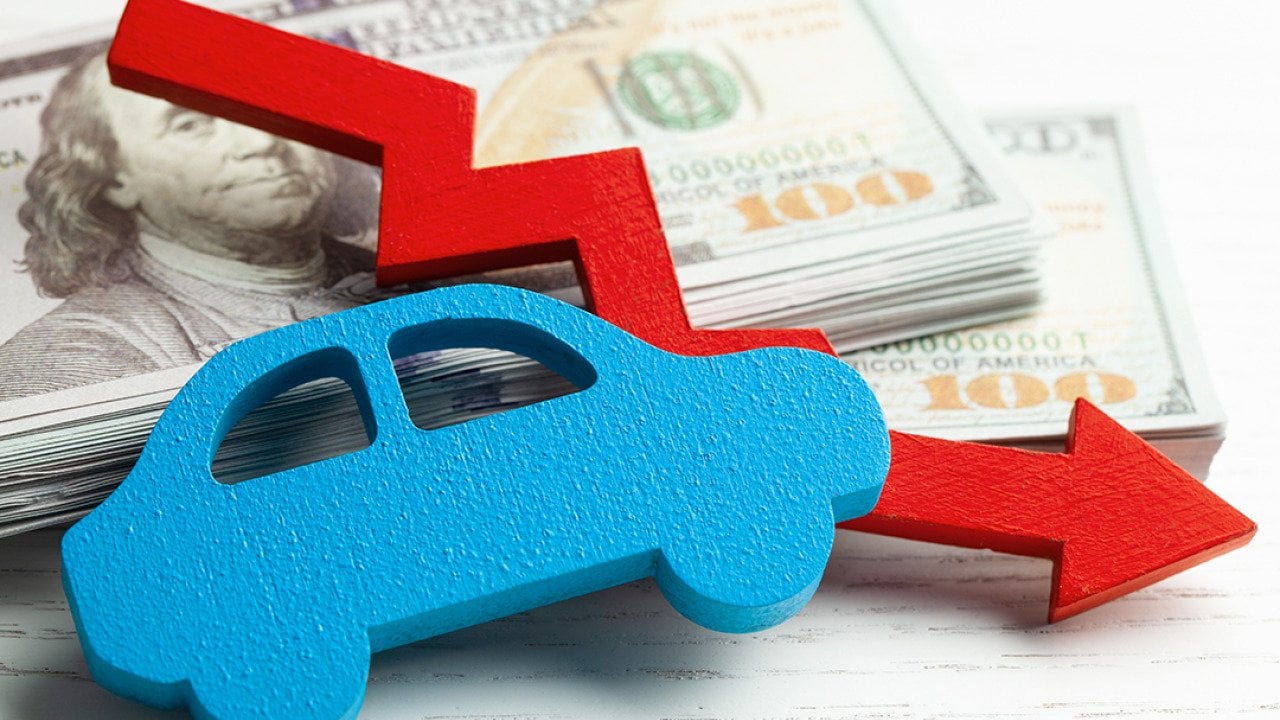 Figure of a car and declining arrow on top of U.S. banknotes.