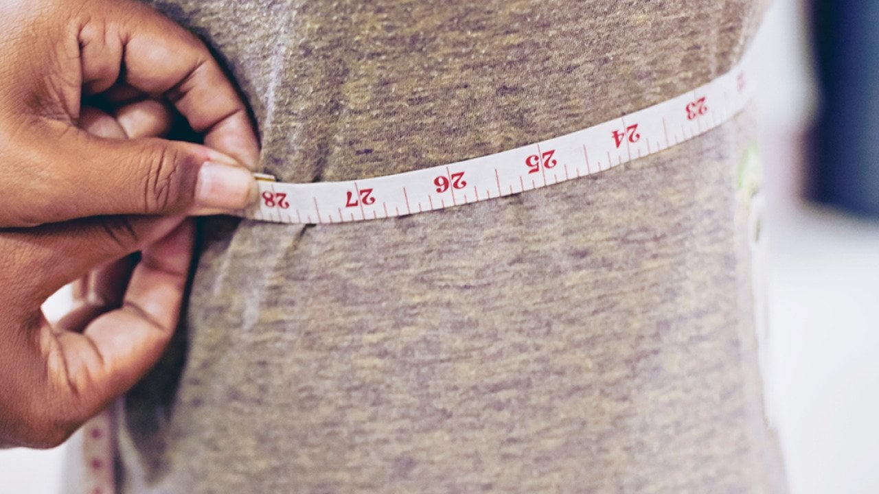 A tailor taking measurements of a client's torso with a tape measure.