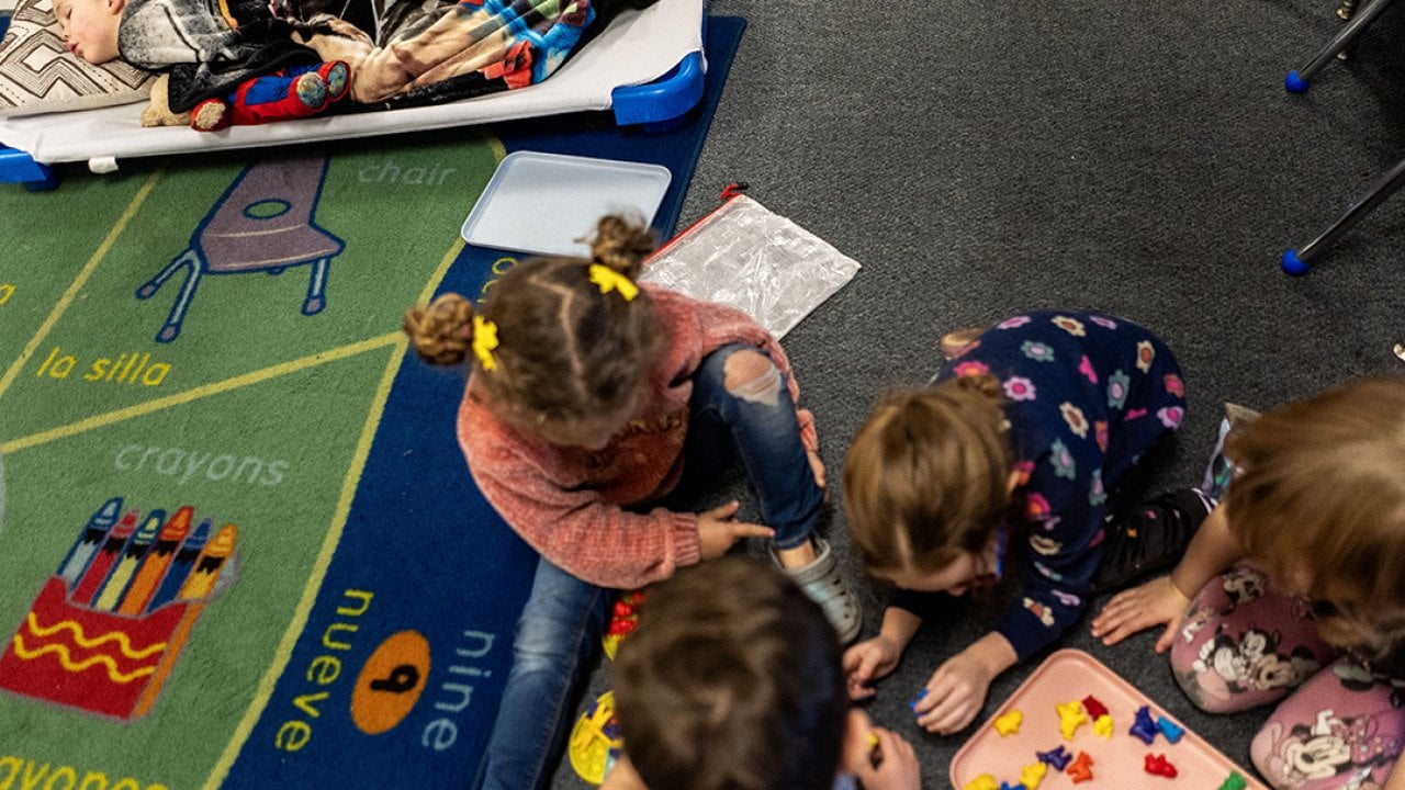 A group of young children during nap time at TLC for Tots daycare center in Nampa, Idaho. One child is sleeping while others are playing.