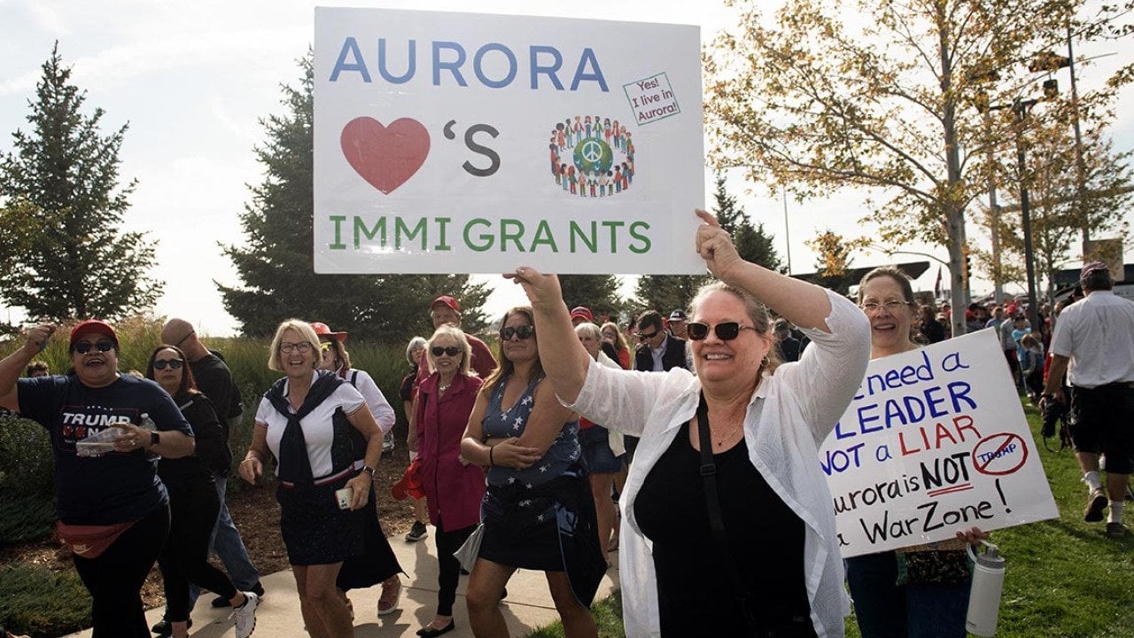 People in Denver protesting the federal government's stance on immigration; one holds a white posterboard that reads 