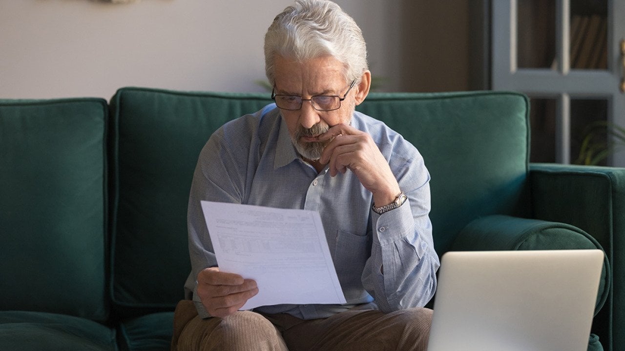 A senior man sitting on a couch intensely analyzing an expense bill.