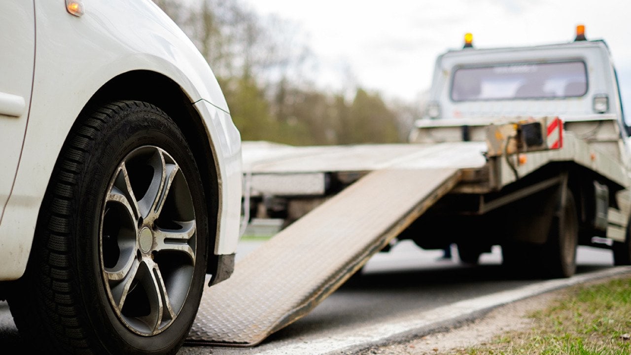 A broken car being loaded on a tow truck on roadside.