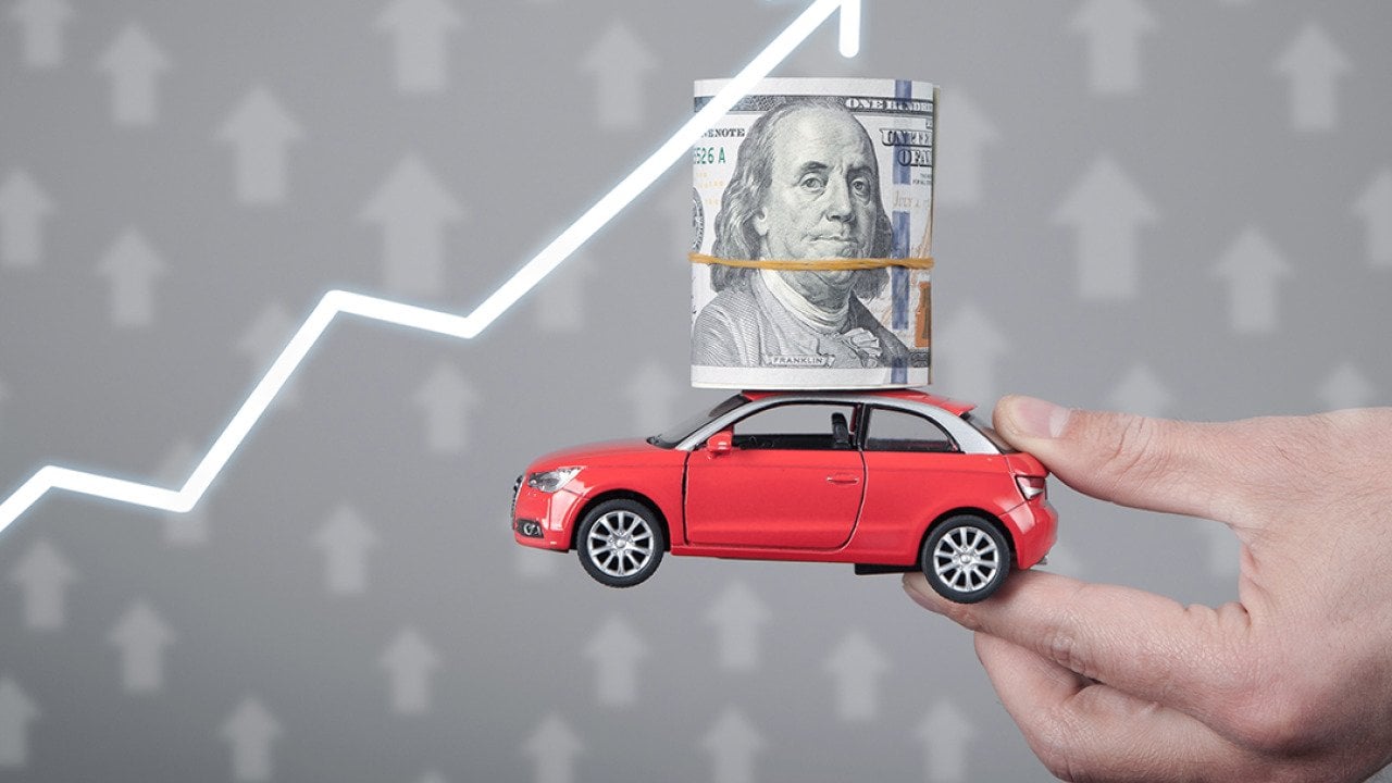 A miniature car with a dollar on top held up with an upward arrow as a concept of rising prices.