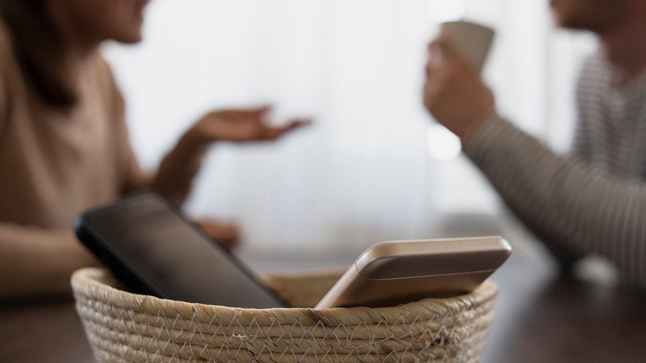 Two phones in a basket with two people catching up in the background.