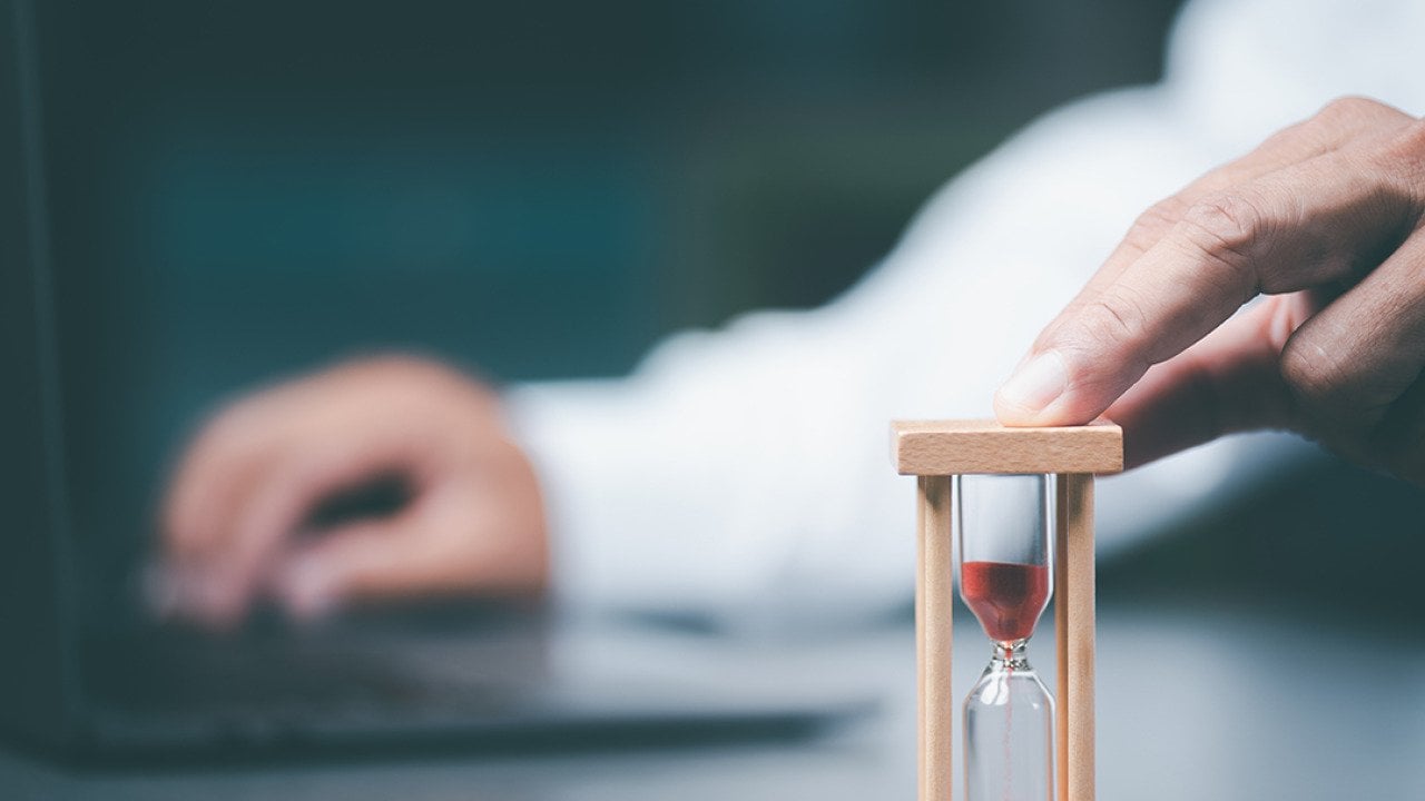 A business employee using a small time hourglass beside a laptop.