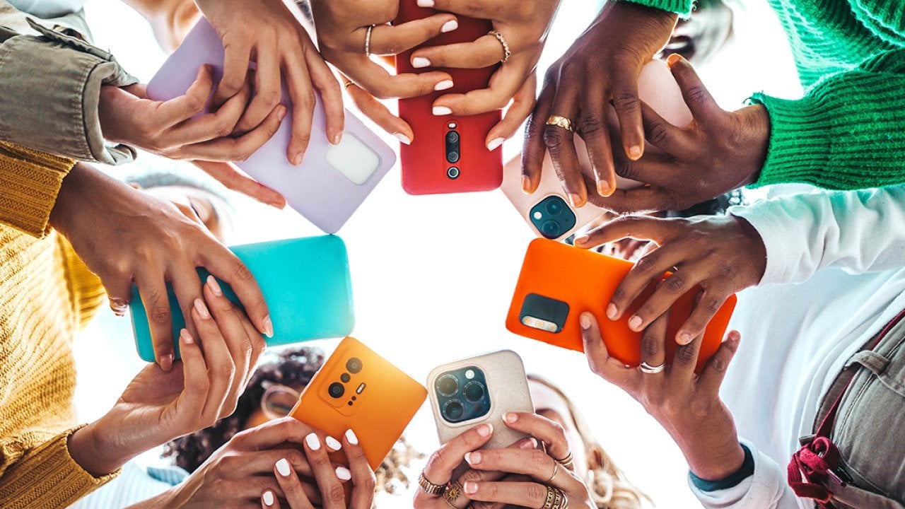 A group of young people using their smartphones outside while forming a circle.