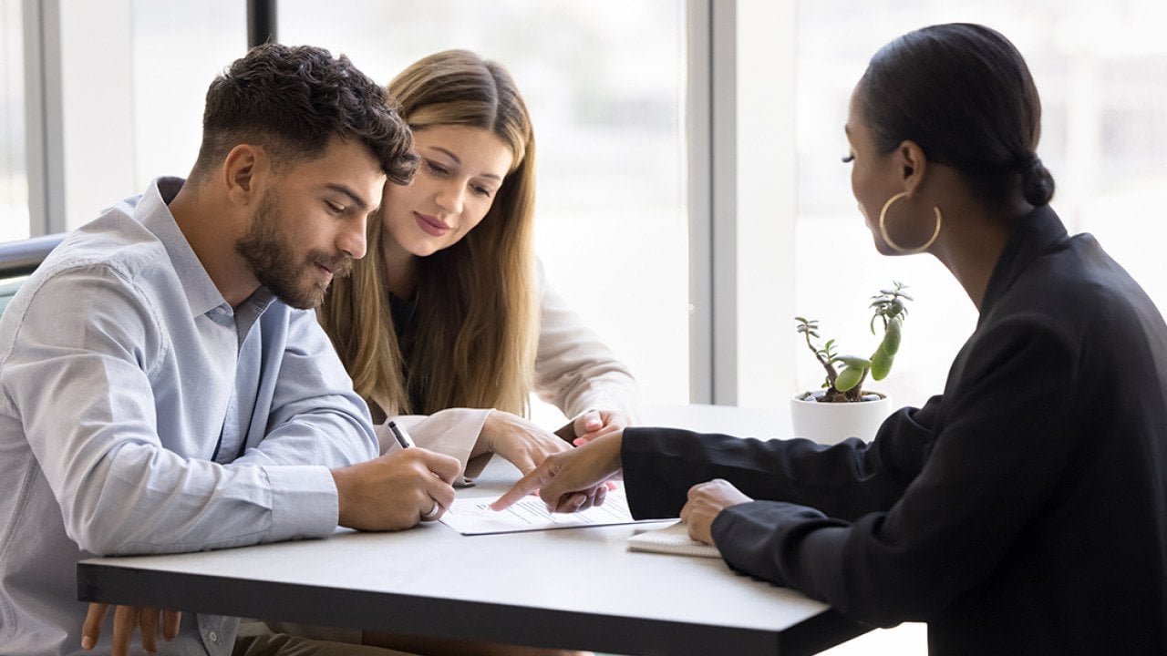 A realtor guiding a couple on signing a property contract.
