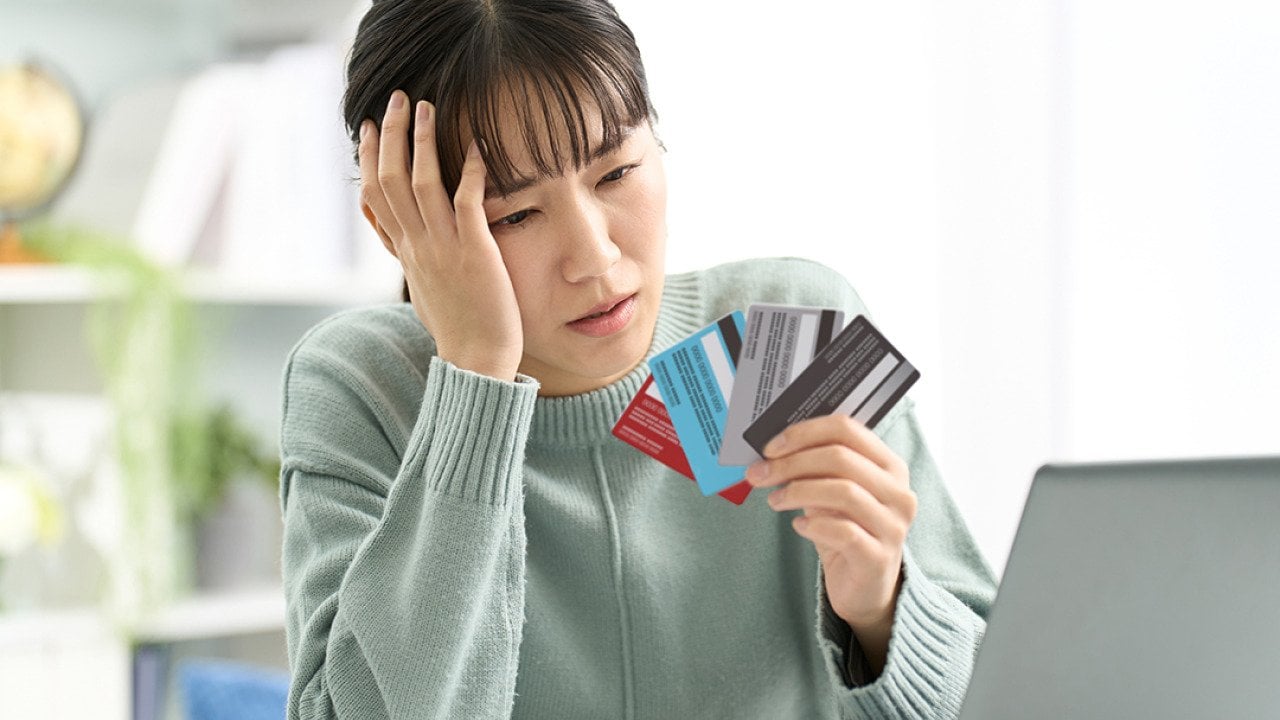 A woman looking worried at her four credit cards.