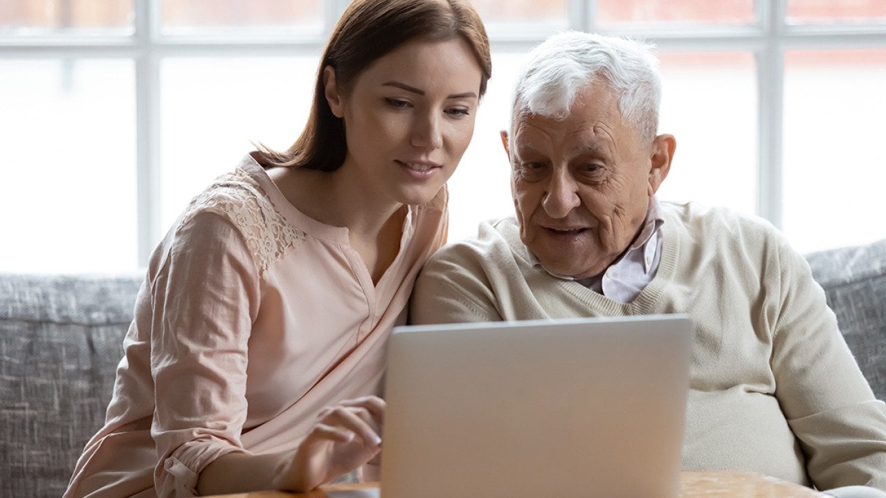 A senior man with his caregiver browsing the internet using a laptop.
