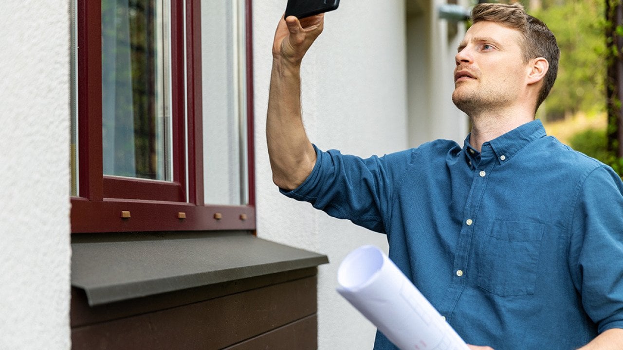 A real estate appraiser takes photo of the outside of a property with his phone.