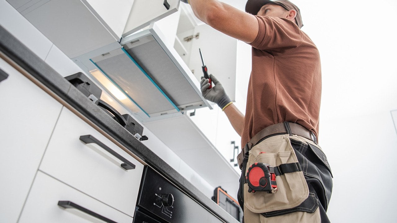 A cabinetmaker finishing a white, modern cabinet installation