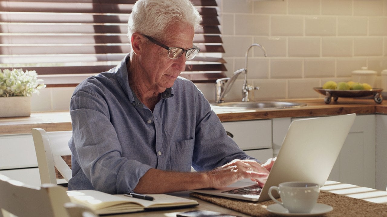 A senior man using a laptop in his kitchen.