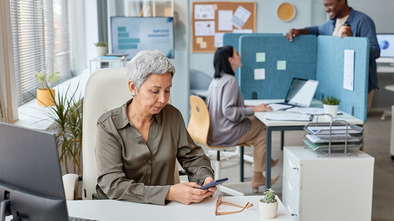 A senior businesswoman working at her desk in an open office setting.