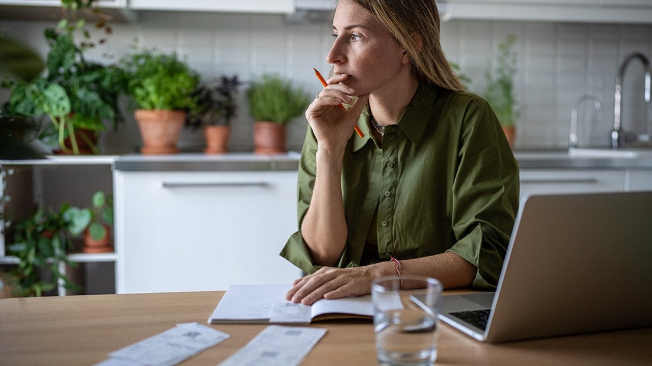 A pensive woman at home working on accounting documents.