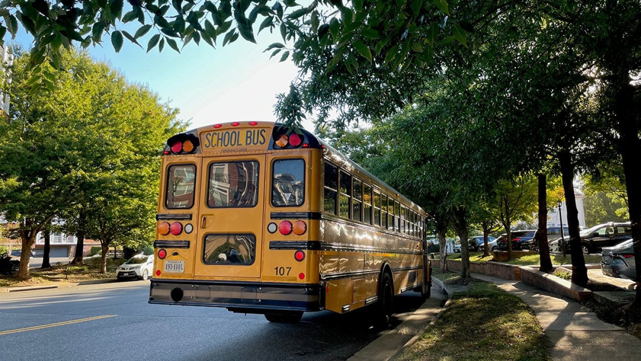 A yellow school bus waits by a bus stop in a family neighborhood in Fairfax County, Virginia.