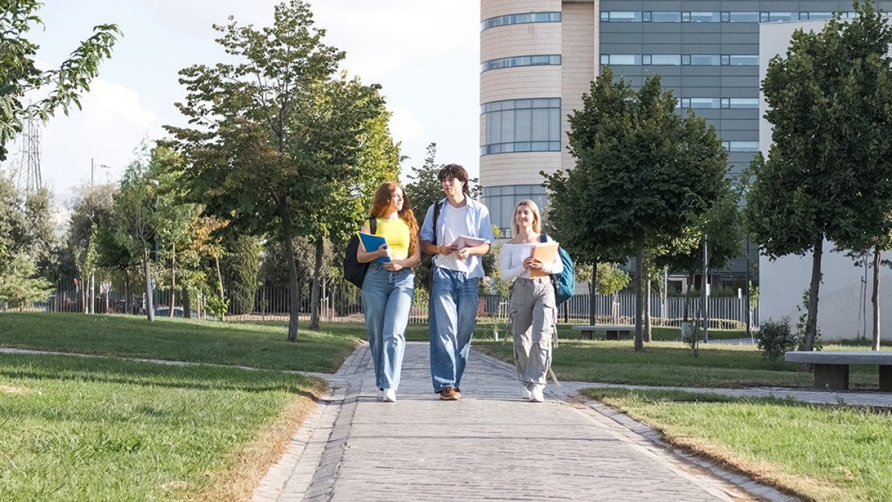 A group of three young college students chatting while walking on university campus footpath.