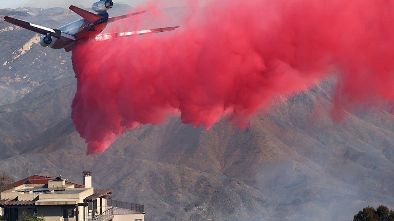 A firefighting aircraft drops the fire retardant Phos-Chek near homes during the Palisades Fire on January 10, 2025 in Topanga, California.