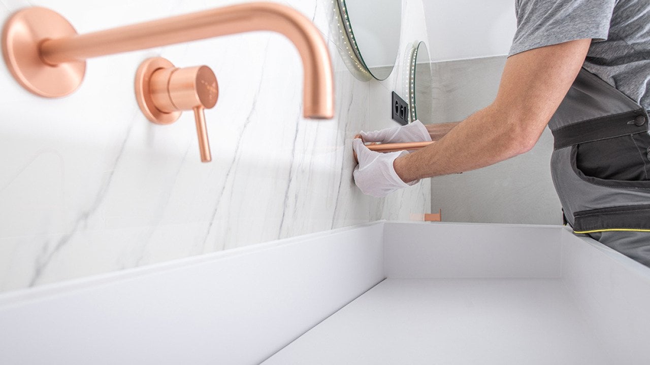 A handyman installs copper faucet to a modern marble wall bathroom.