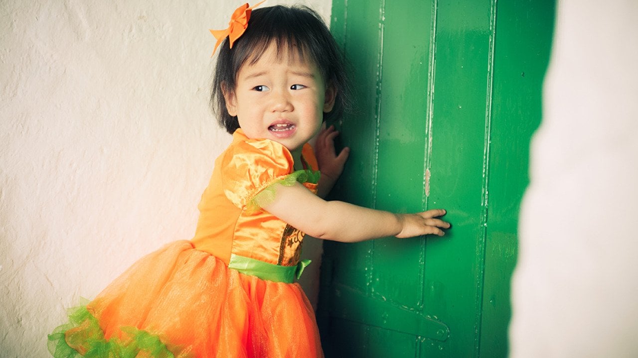 A young girl wearing an orange Halloween dress crying during a party.