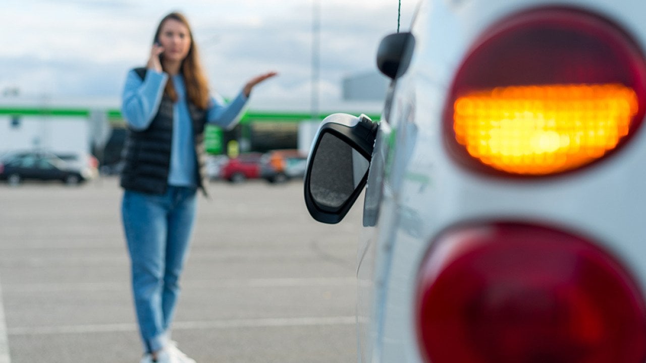 Woman talking on her phone while looking at her car's broken left side rear-view mirror.