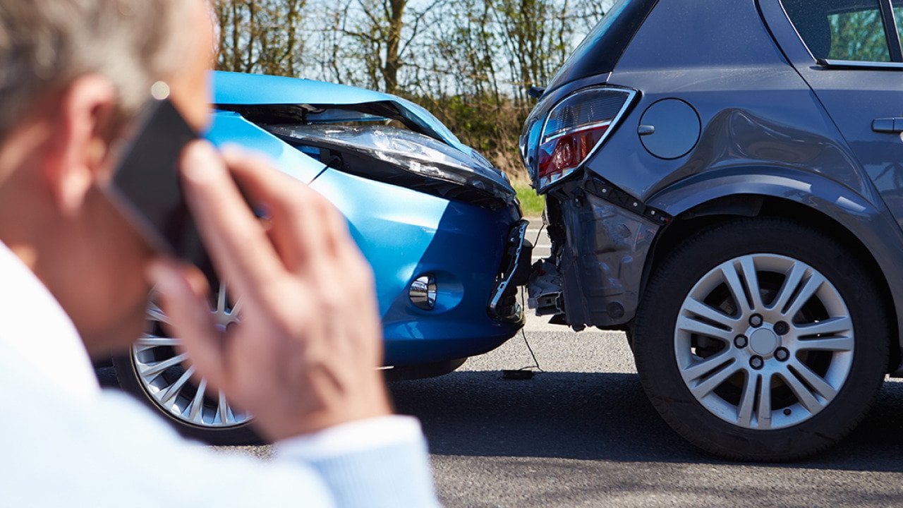 A car driver talks on the phone while looking at a rear-end collision.
