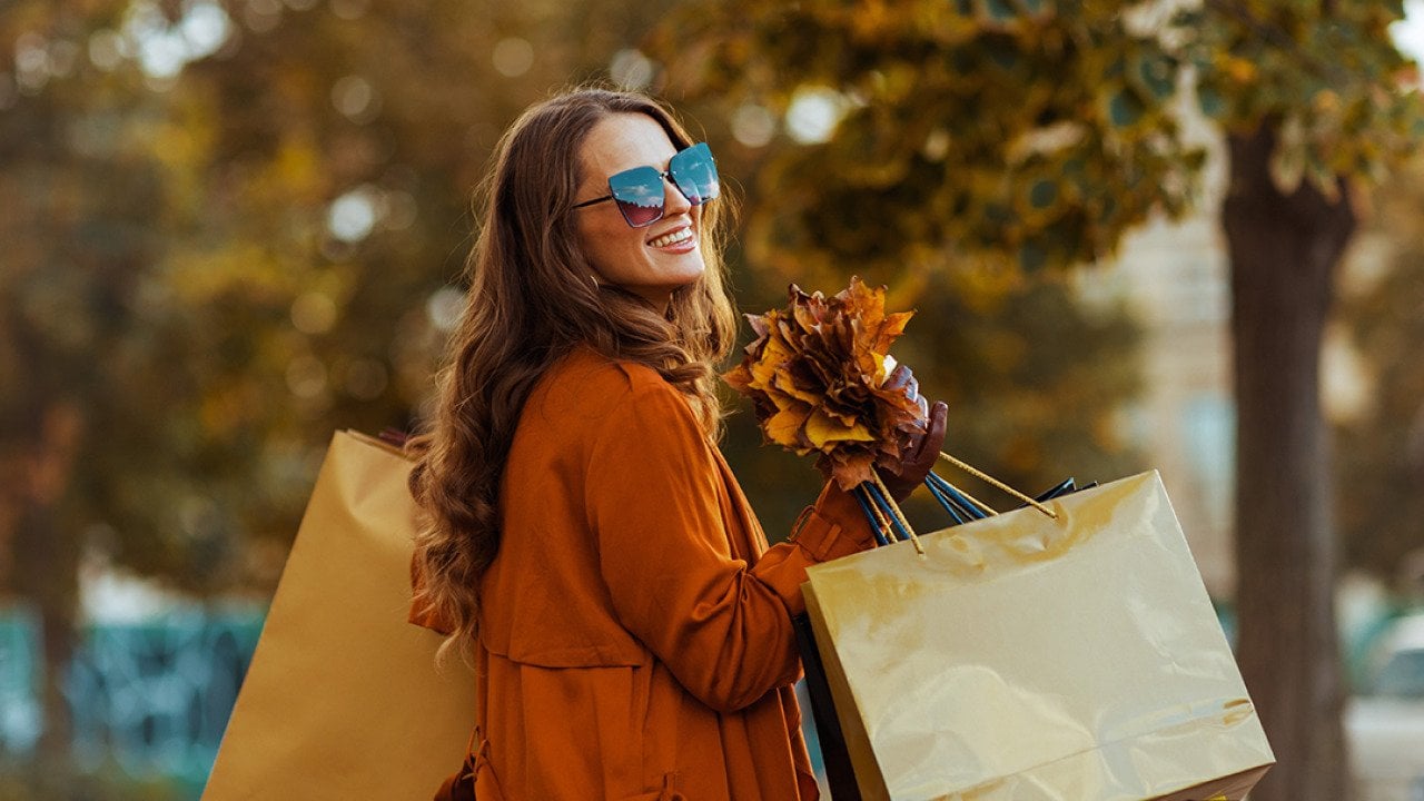A happy stylish woman holding shopping bags and autumn leaves.