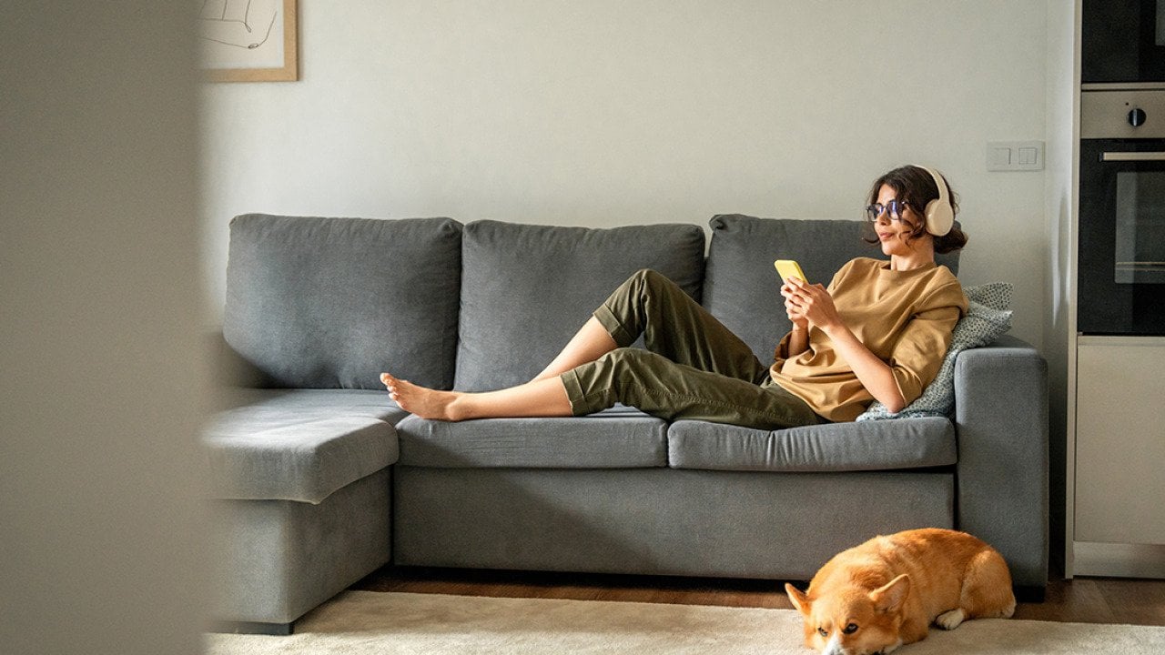 A young woman lying on couch while listening to music with her headphones.