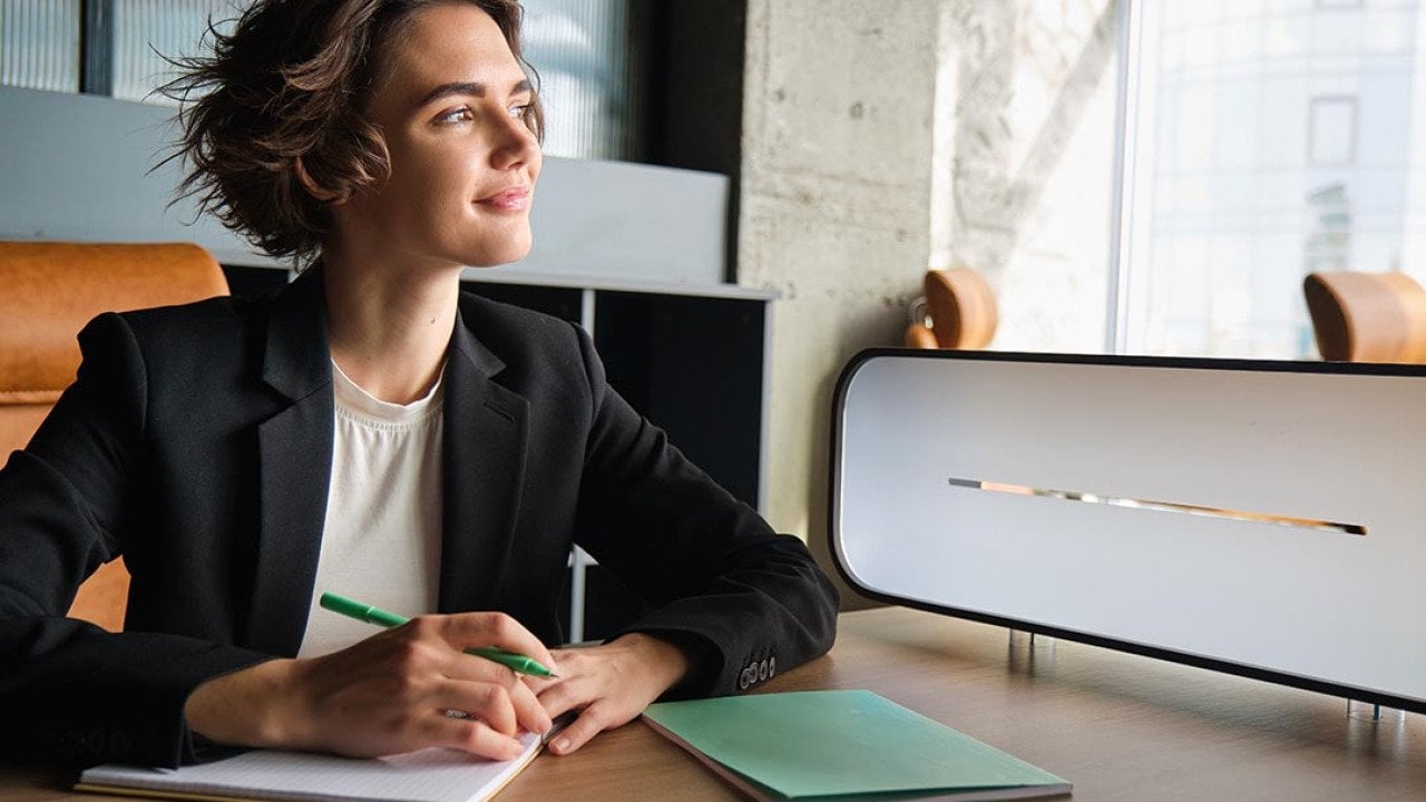 Business woman in office looks toward window thinking while taking notes.