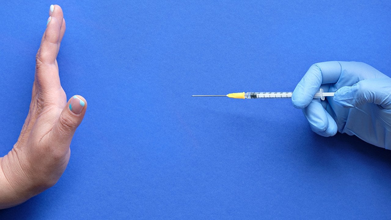 A hand refusing to receive a vaccine syringe.