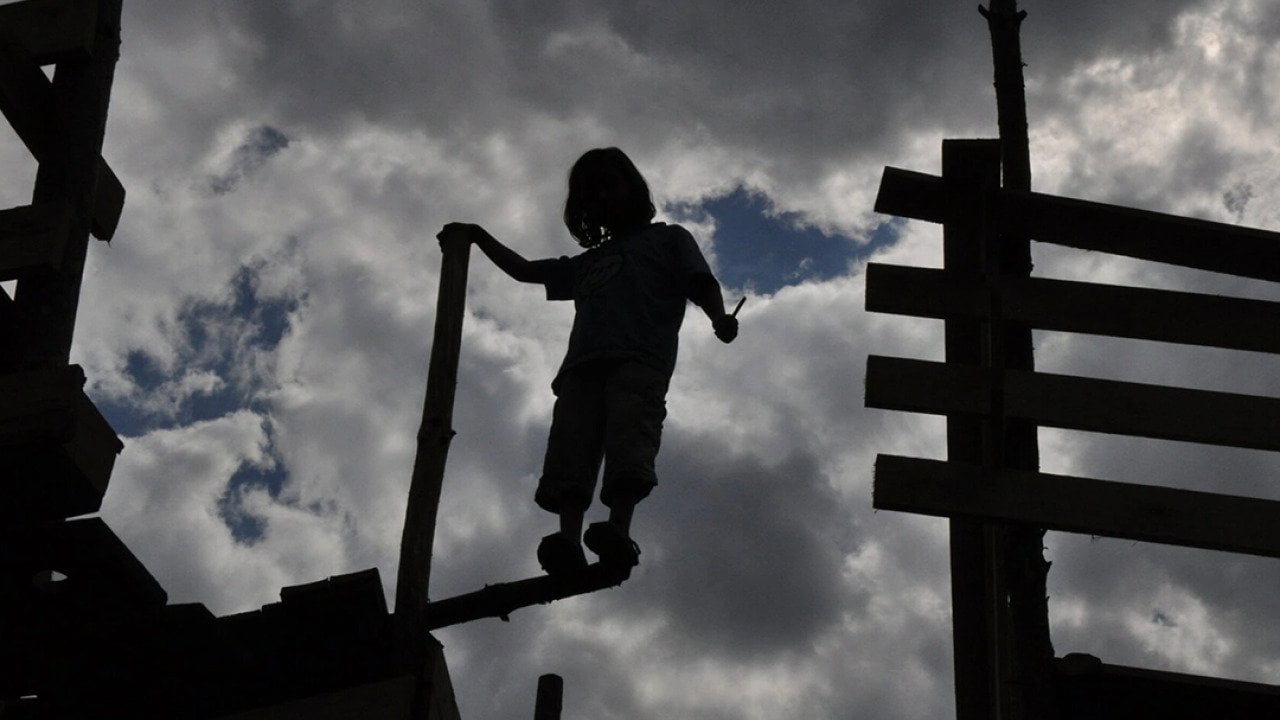 Silhouette of one of the children standing on the edge of an abandoned wooden fort.